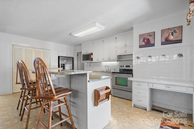 kitchen featuring a center island, light floors, stainless steel appliances, white cabinets, and a kitchen breakfast bar