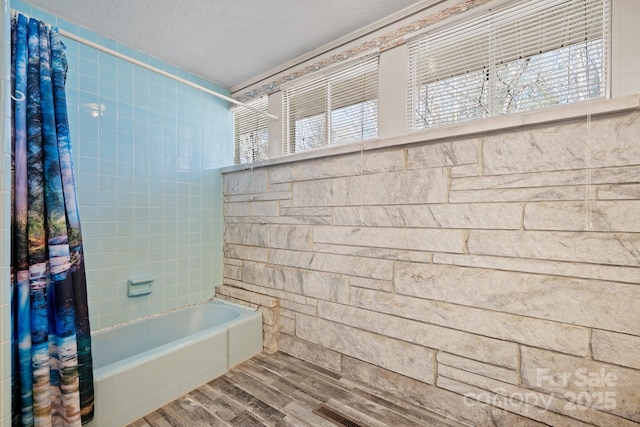 bathroom featuring a textured ceiling, wood finished floors, and shower / bath combo with shower curtain