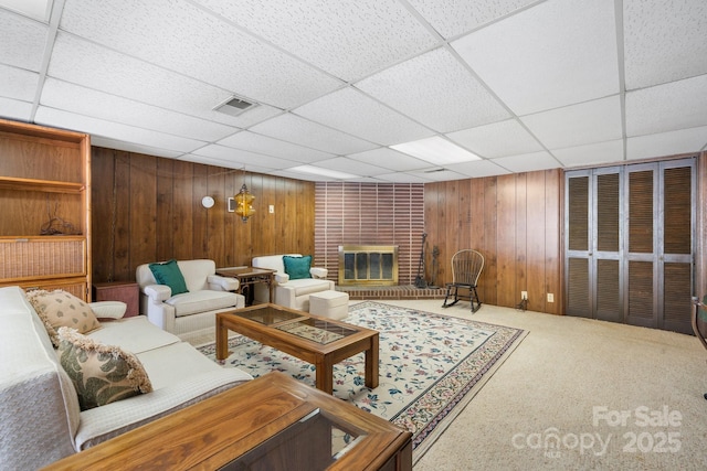 living area featuring a drop ceiling, wood walls, a fireplace, carpet flooring, and visible vents