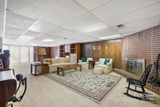 living room featuring a paneled ceiling, a brick fireplace, visible vents, and wooden walls