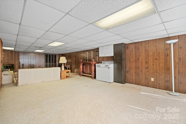 finished below grade area featuring a paneled ceiling, wooden walls, carpet, and a fireplace