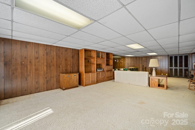 finished below grade area with carpet floors, a drop ceiling, a brick fireplace, and wooden walls