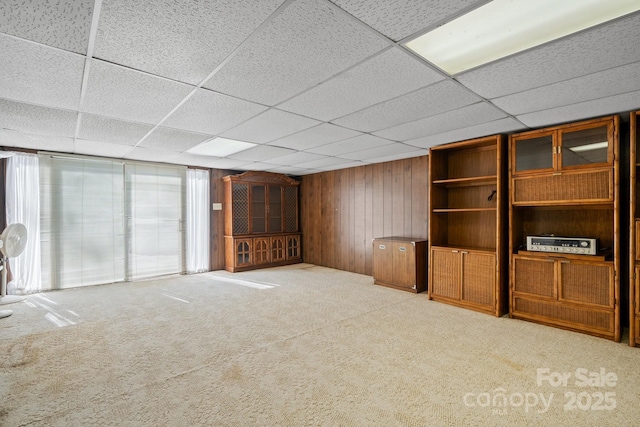 unfurnished living room featuring wood walls, a drop ceiling, and light colored carpet