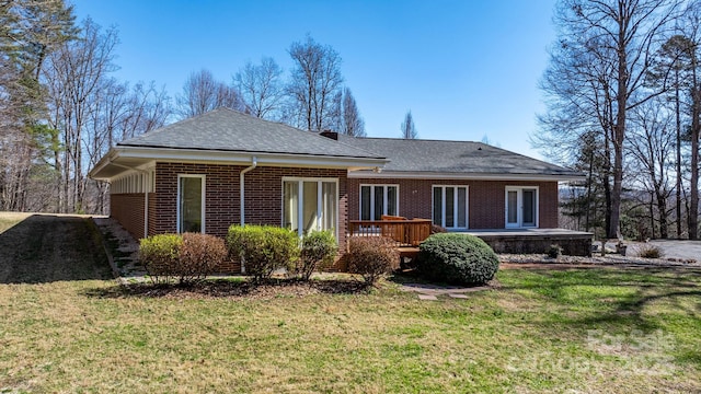 back of house featuring a deck, brick siding, a lawn, and a shingled roof