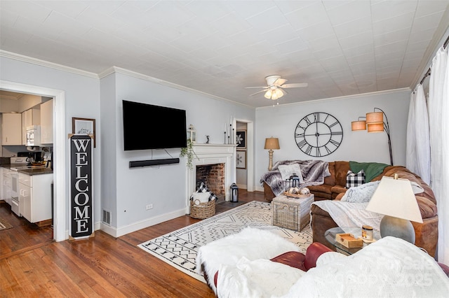 living room featuring baseboards, a ceiling fan, ornamental molding, dark wood-style flooring, and a fireplace