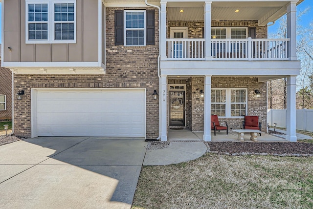 view of front of house featuring a balcony, a garage, brick siding, driveway, and board and batten siding