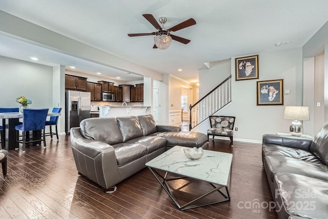 living room with ceiling fan, stairs, baseboards, and dark wood-style flooring