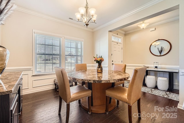 dining space with crown molding, dark wood finished floors, a notable chandelier, a decorative wall, and wainscoting