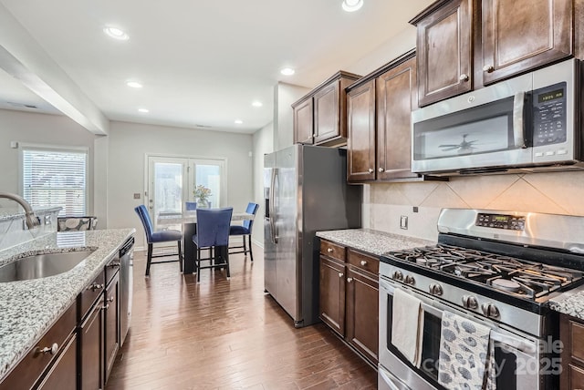 kitchen featuring light stone counters, dark wood finished floors, appliances with stainless steel finishes, a sink, and dark brown cabinets