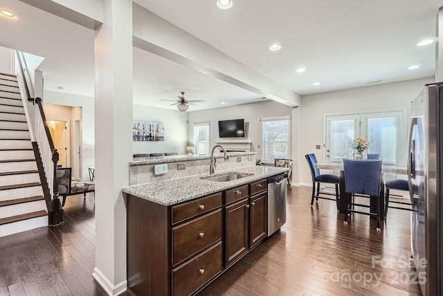 kitchen featuring light stone counters, dark brown cabinetry, a sink, appliances with stainless steel finishes, and dark wood finished floors