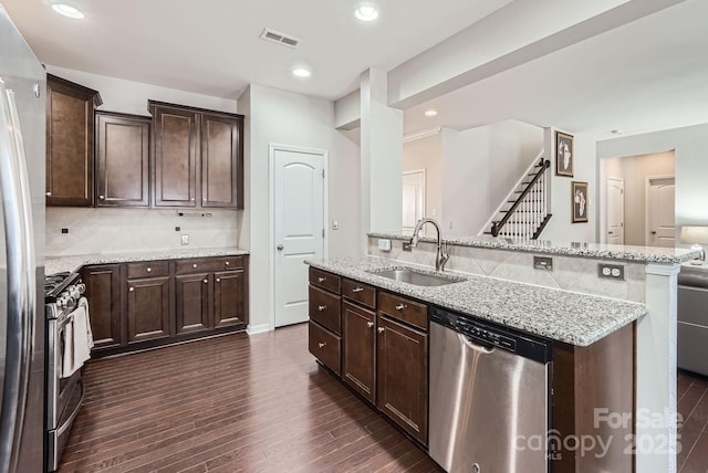 kitchen featuring dark brown cabinetry, stainless steel appliances, dark wood-type flooring, a sink, and light stone countertops