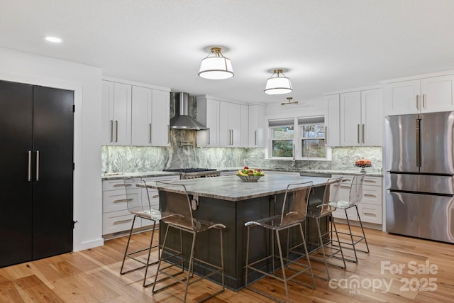 kitchen featuring appliances with stainless steel finishes, light wood-style floors, wall chimney range hood, and a kitchen breakfast bar