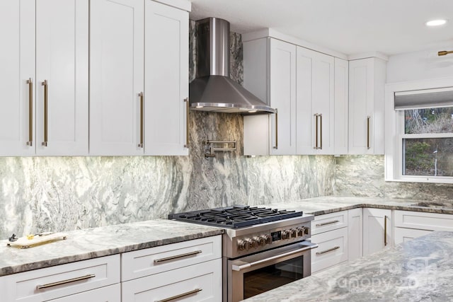 kitchen with wall chimney exhaust hood, light stone counters, high end range, and decorative backsplash