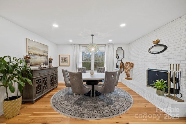 dining area with brick wall, light wood-style flooring, a fireplace, a notable chandelier, and recessed lighting