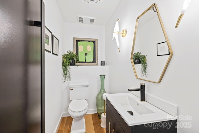 half bathroom with visible vents, vanity, toilet, and wood finished floors