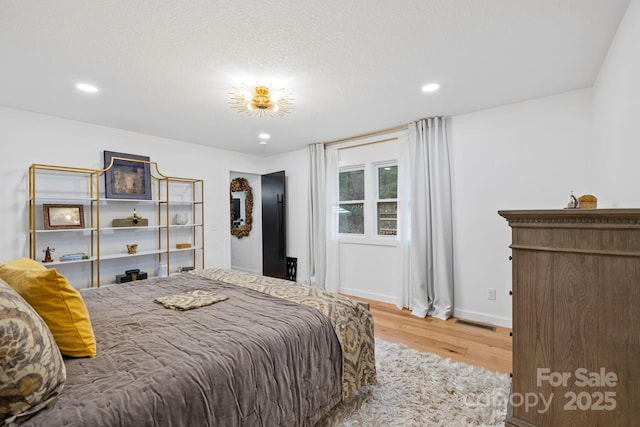 bedroom featuring recessed lighting, visible vents, a textured ceiling, wood finished floors, and baseboards