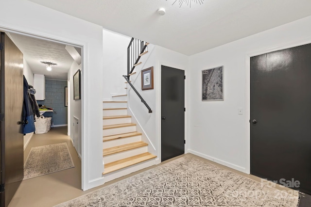 foyer entrance featuring stairway, a textured ceiling, and baseboards