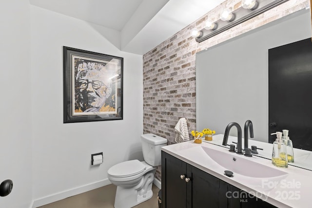 bathroom featuring brick wall, vanity, toilet, and baseboards