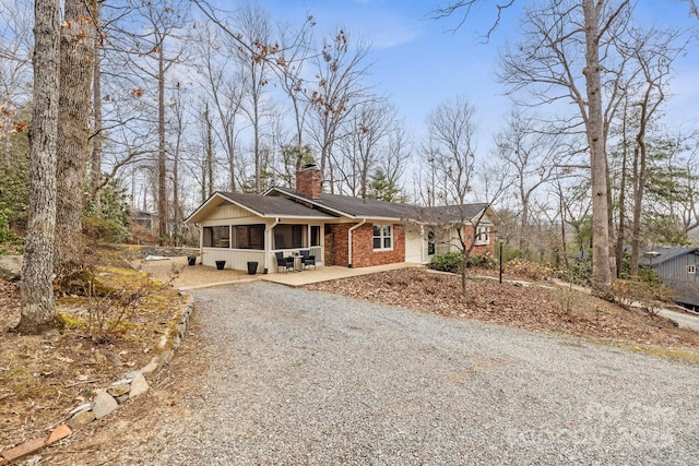 single story home with driveway, a sunroom, a chimney, and brick siding