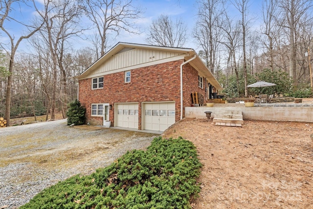 view of side of property with board and batten siding, brick siding, dirt driveway, and an attached garage