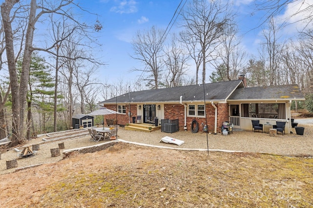 back of property featuring brick siding, an outdoor structure, a sunroom, a storage unit, and a chimney