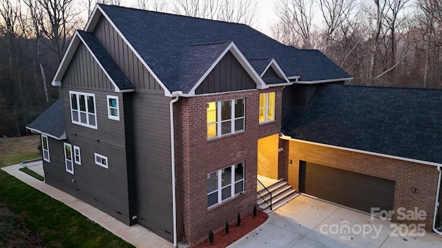 view of front facade featuring a garage, a shingled roof, board and batten siding, and brick siding