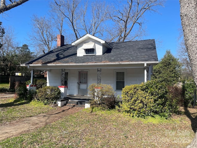 bungalow-style house featuring a shingled roof, a chimney, a front lawn, and a porch