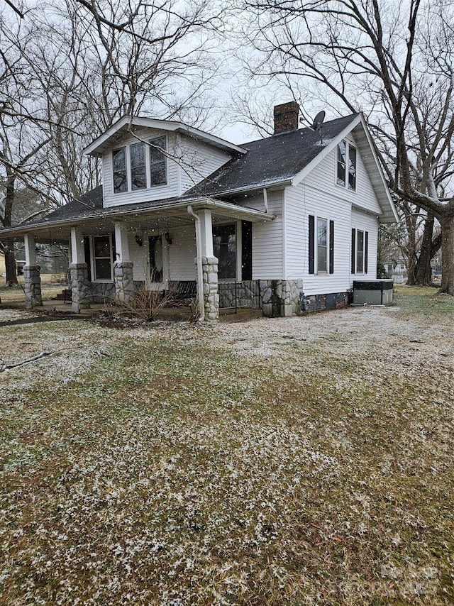 view of front facade featuring stone siding, a shingled roof, a chimney, and a porch