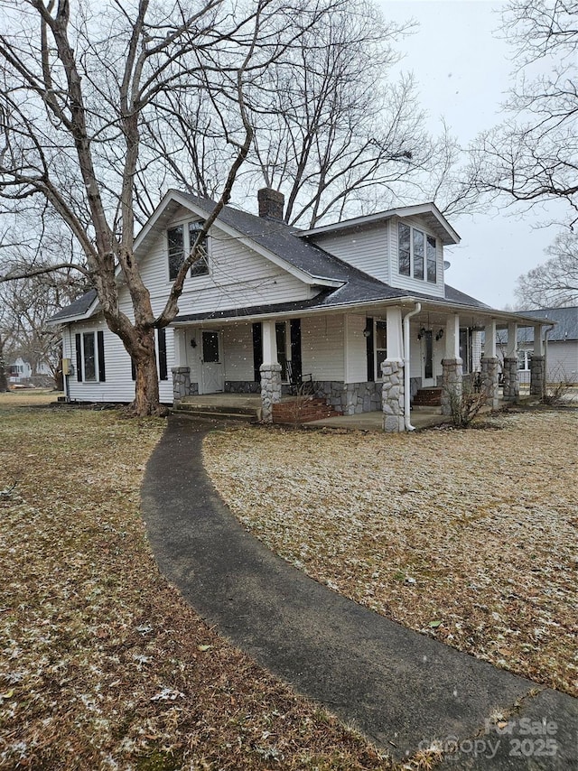 view of front of property featuring stone siding, a chimney, and a porch