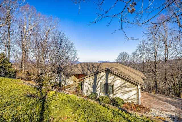 view of side of property featuring driveway and a shingled roof