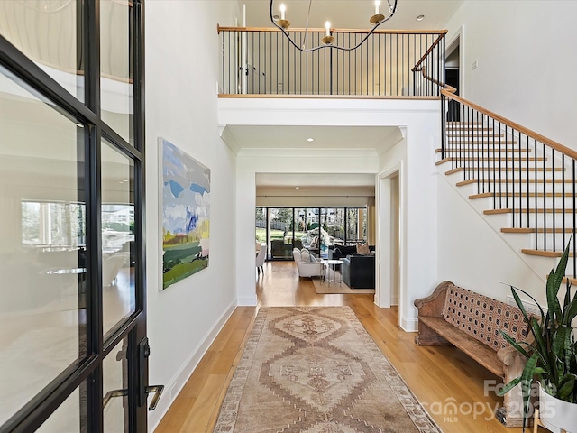 foyer entrance featuring baseboards, a high ceiling, wood finished floors, and an inviting chandelier