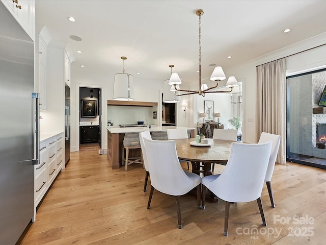 dining space featuring crown molding, light wood-type flooring, a fireplace, and recessed lighting