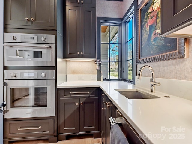 kitchen with a sink, dark brown cabinetry, light countertops, and stainless steel double oven