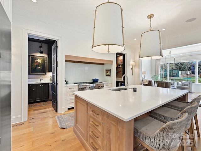 kitchen with decorative light fixtures, light countertops, a sink, an island with sink, and light wood-type flooring