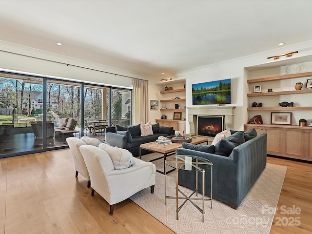 living area with a warm lit fireplace, light wood-style flooring, built in shelves, and recessed lighting