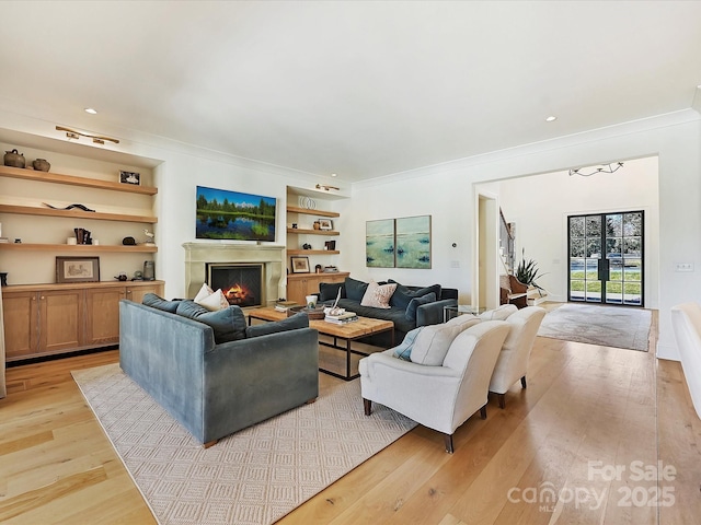 living area with ornamental molding, light wood finished floors, a warm lit fireplace, and built in shelves