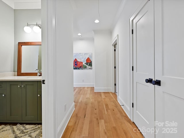 hall with light wood-style flooring, recessed lighting, a sink, baseboards, and ornamental molding