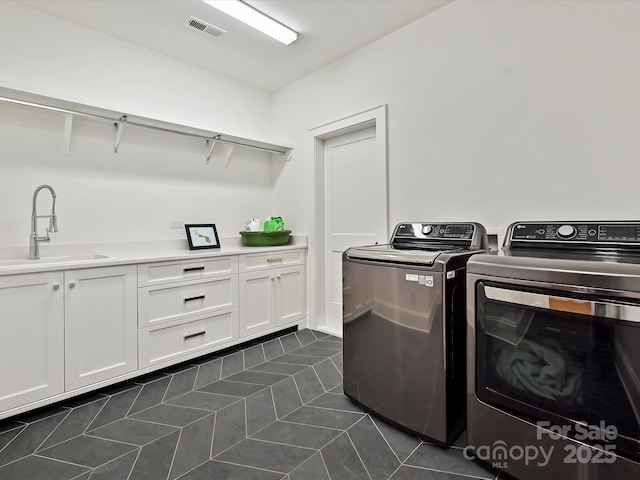 washroom featuring dark tile patterned floors, a sink, visible vents, washer and dryer, and cabinet space