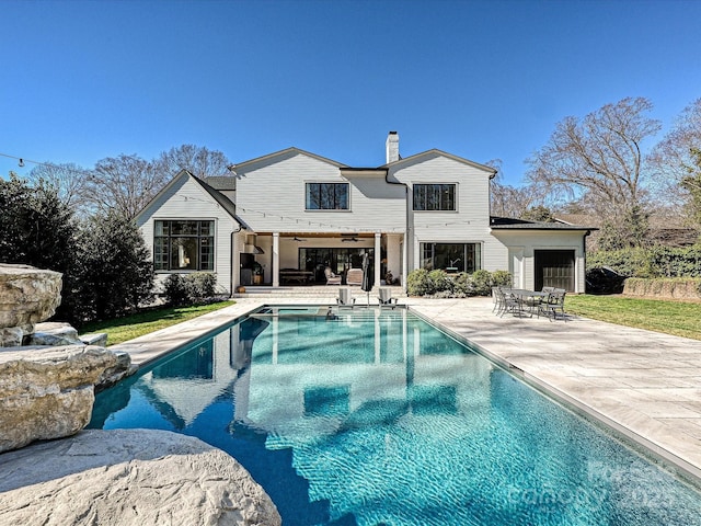 rear view of house with outdoor dining area, a patio, a chimney, ceiling fan, and an outdoor pool