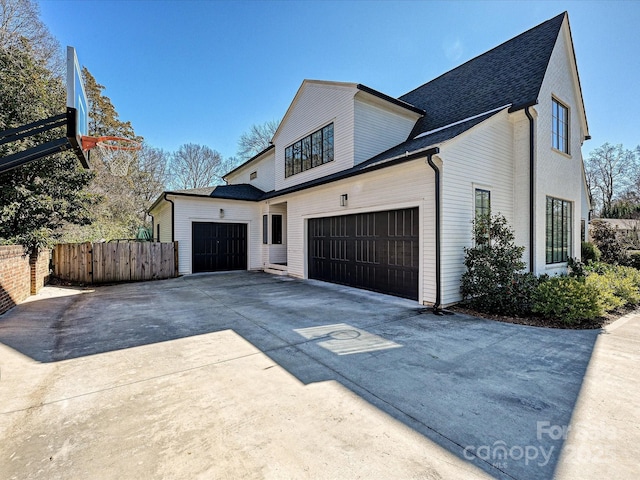 view of side of property with driveway, a garage, fence, and roof with shingles