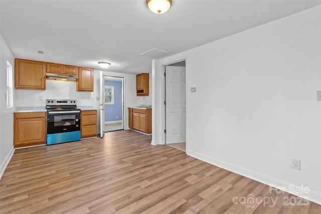 kitchen with brown cabinets, light countertops, light wood-style floors, stainless steel range with electric cooktop, and under cabinet range hood