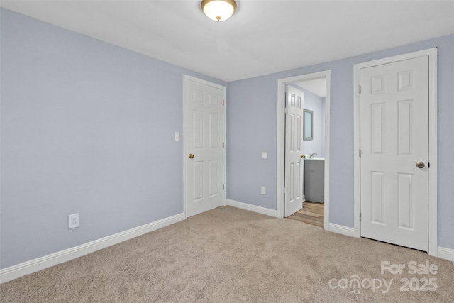 unfurnished bedroom with light carpet, ensuite bath, and baseboards