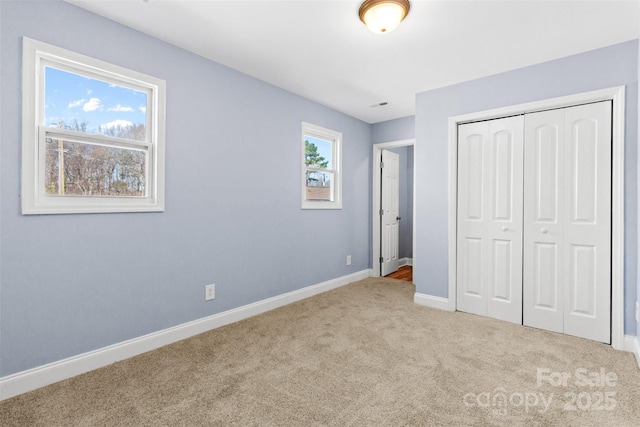 unfurnished bedroom featuring multiple windows, baseboards, a closet, and light colored carpet