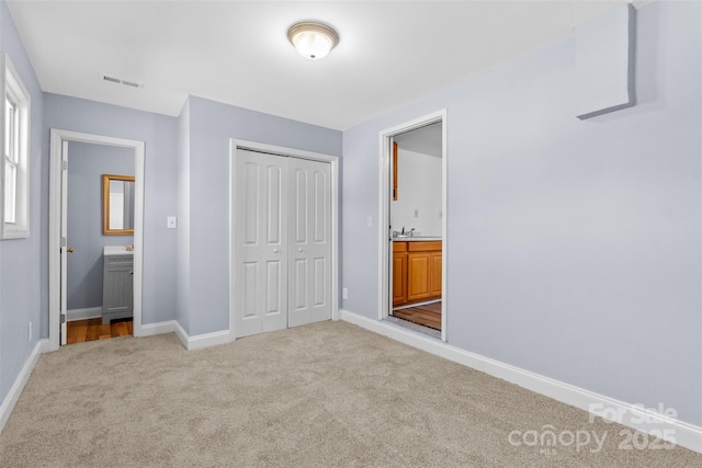 unfurnished bedroom featuring a closet, light colored carpet, visible vents, connected bathroom, and baseboards