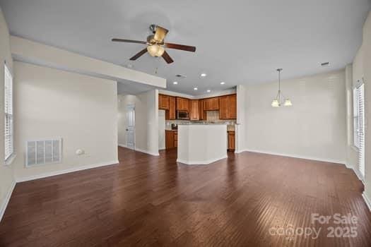 unfurnished living room with recessed lighting, ceiling fan with notable chandelier, visible vents, baseboards, and dark wood-style floors