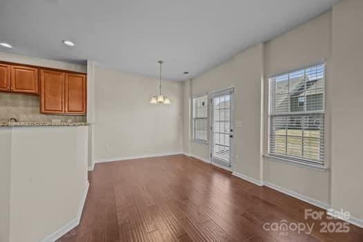 unfurnished dining area with baseboards, dark wood-type flooring, and a notable chandelier