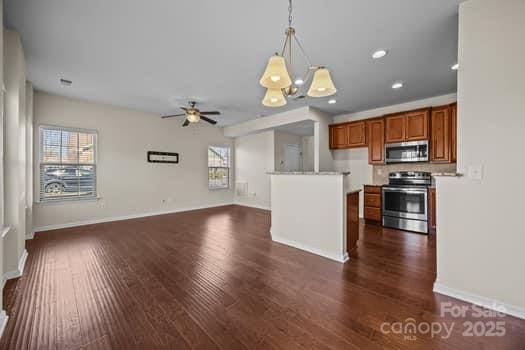 kitchen with open floor plan, appliances with stainless steel finishes, brown cabinets, dark wood-style floors, and decorative light fixtures