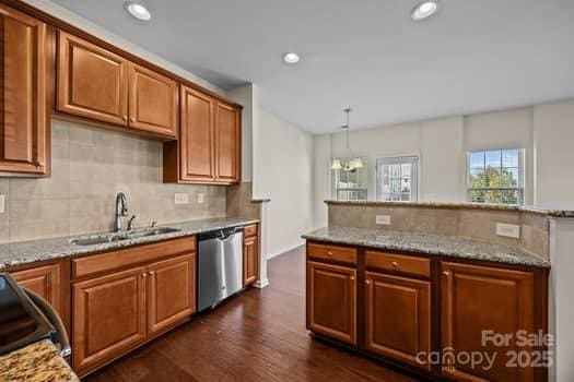 kitchen with light stone counters, brown cabinets, dishwasher, and a sink