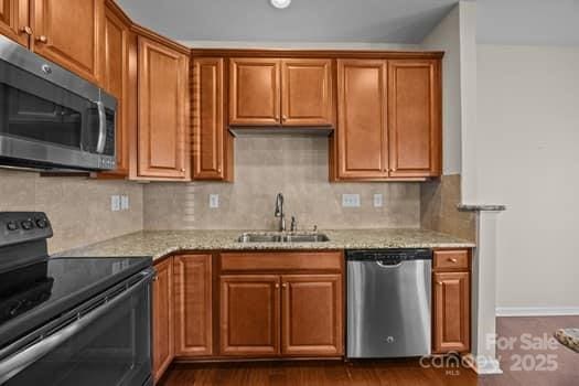 kitchen featuring light stone countertops, appliances with stainless steel finishes, brown cabinets, and a sink