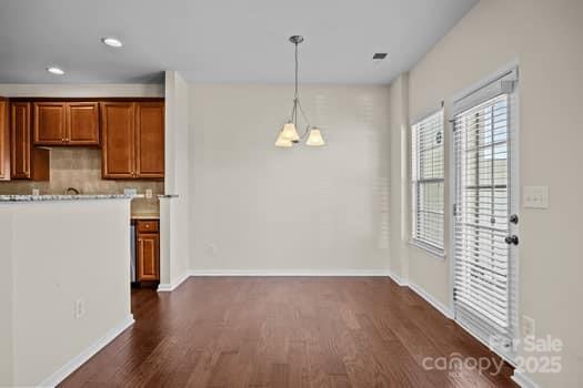 kitchen featuring dark wood-style flooring, brown cabinets, light countertops, backsplash, and an inviting chandelier